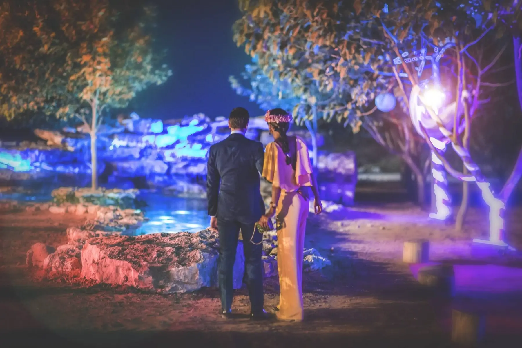 The couple from behind beside the waterfall and pond lit blue