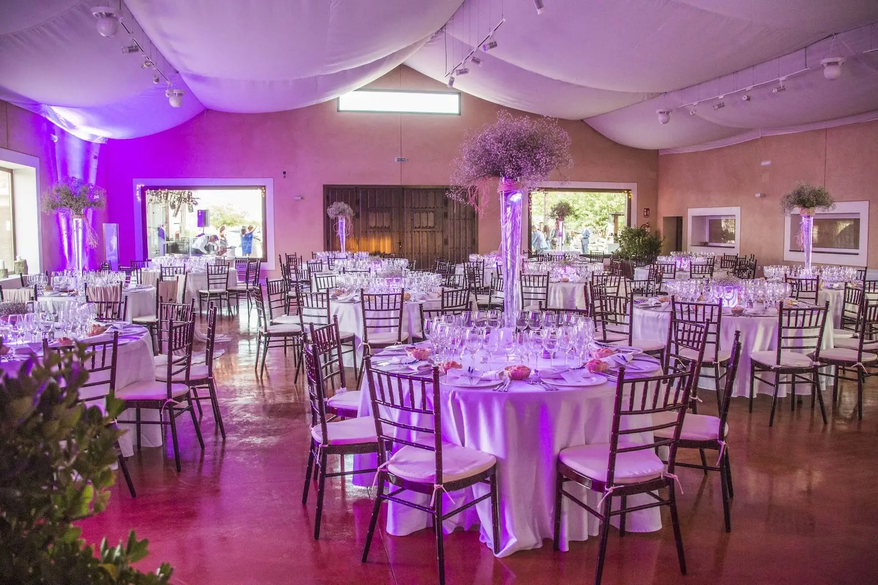 El salón cubierto con techo de tela blanca, mesas redondas con jarrones altos de flores y luz violeta